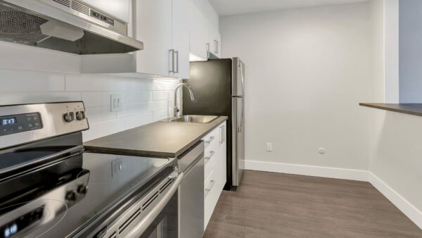 Kitchen with wood floor, white cabinets, stainless steel appliances, and opening to living area.