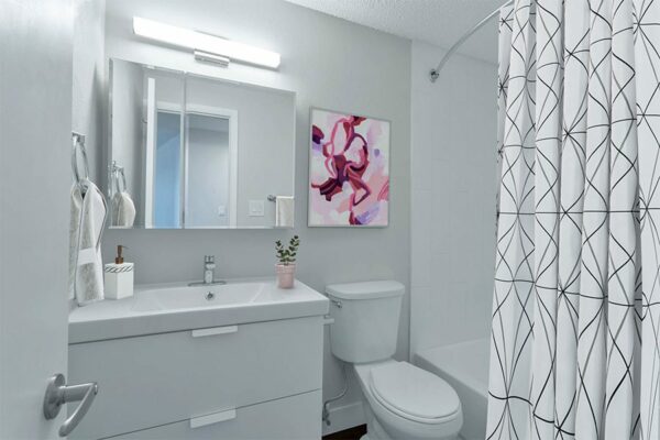 Apartment bathroom with white cabinets and sink, large mirror, and tiled shower tub.
