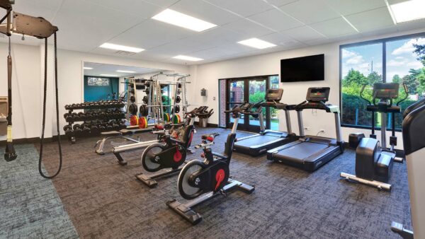Fitness center with carpet, cardio machines, weight equipment, wall mounted TV, and large windows.