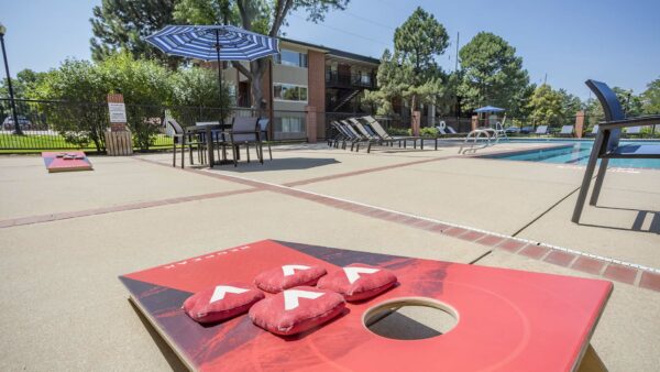 Pool area with lounge chairs, tables with umbrellas, and corn hole game.
