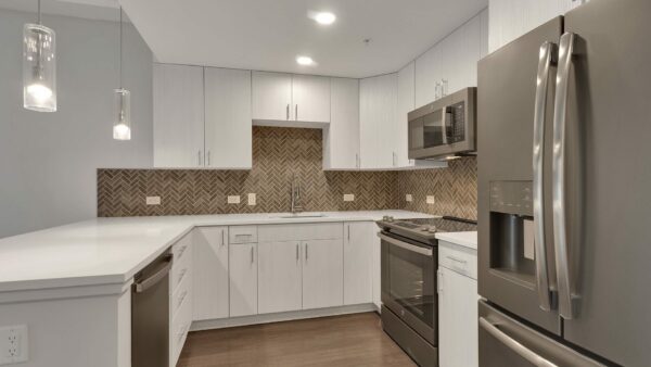 Kitchen with wood floor, white cabinets, tiled backsplash, and stainless steel appliances.