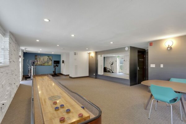 Lounge with shuffleboard table and cardio machines.