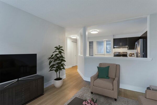 Living area with wood floors and white walls looking into the kitchen.