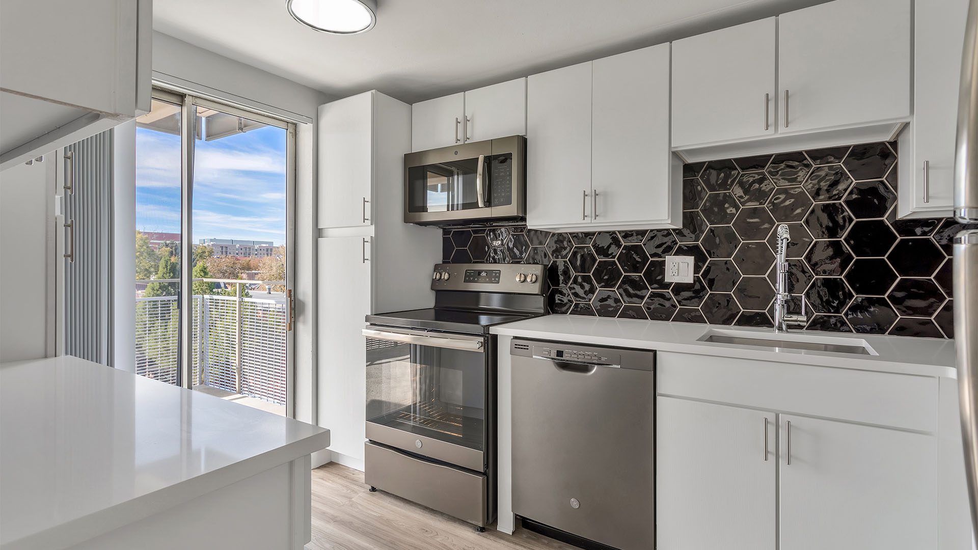 Kitchen with wood floor, white cabinets and counters, stainless steel appliances, and door to balcony.