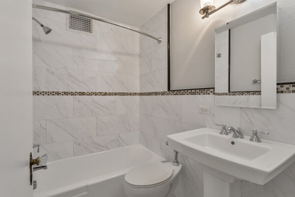 Bathroom with tiled walls, pedestal sink, and tiled shower tub.