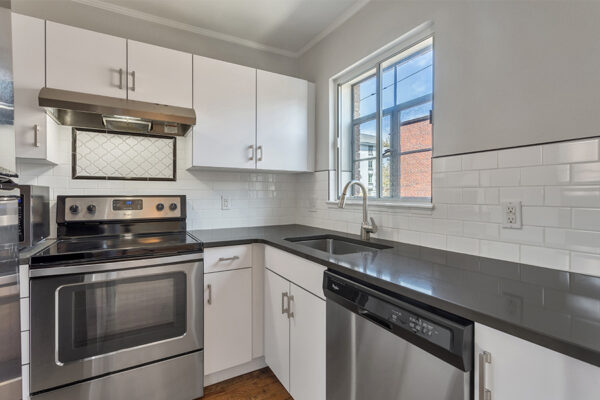 Kitchen with white cabinets, dark counters, stainless steel appliances, and window over sink.