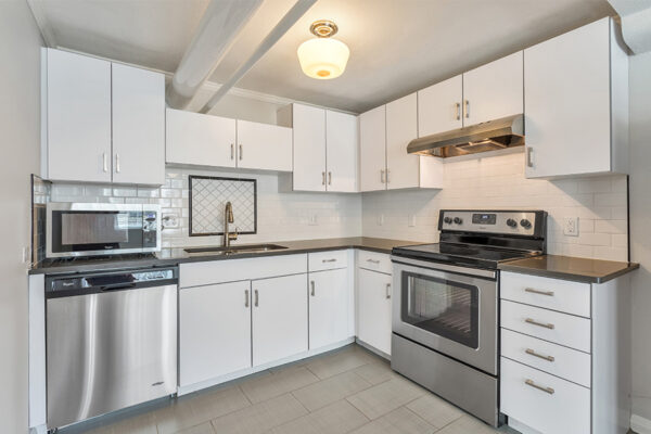Kitchen with tile floor, white cabinets, dark counters, and stainless steel appliances.