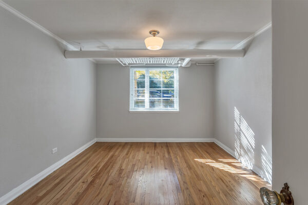 Bedroom with wood floor, cool gray walls with white trim, and large window.
