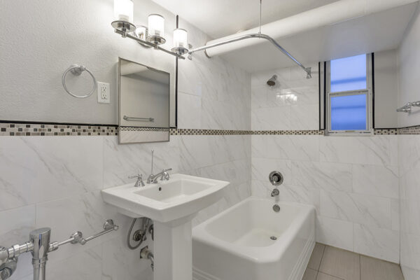 Bathroom with tiled walls, pedestal sink, and shower tub with curtain rod.