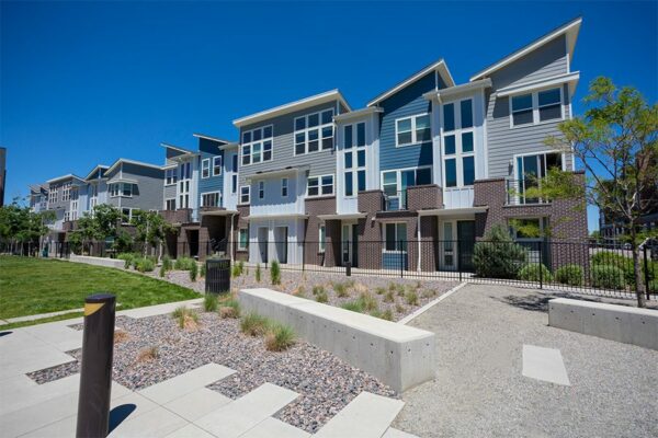 Platt Park townhomes with lush green lawns, iron fence, tall trees, and outdoor seating area. .