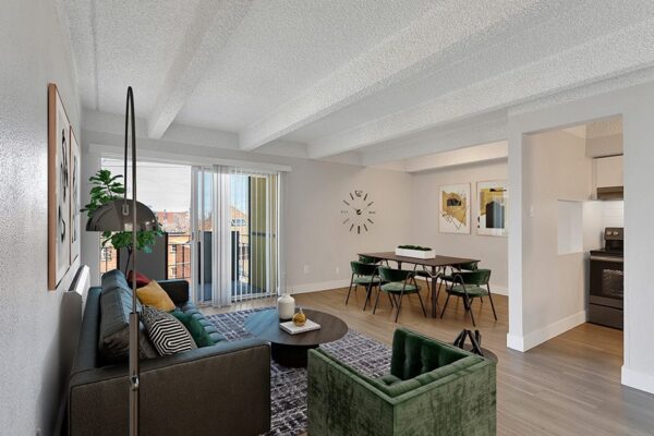 Living area with carpet over laminate flooring, a plush couch and arm chair, and a dining table with 4 chairs.