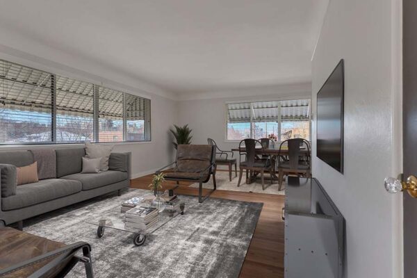 Furnished living room with a large carpet over wood floors, multiple windows, and white walls.