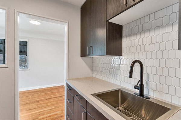 Kitchen with dark cabinets, light counters, stainless steel sink, tiled backsplash, and door to dining room.