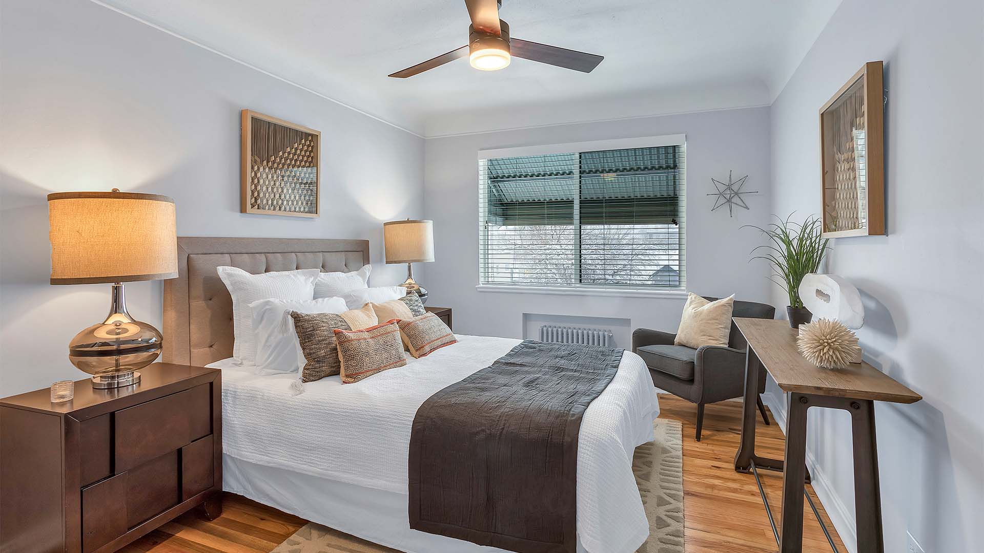Bedroom with plush bed with headboard, rich wood furniture, ceiling fan, and large window.