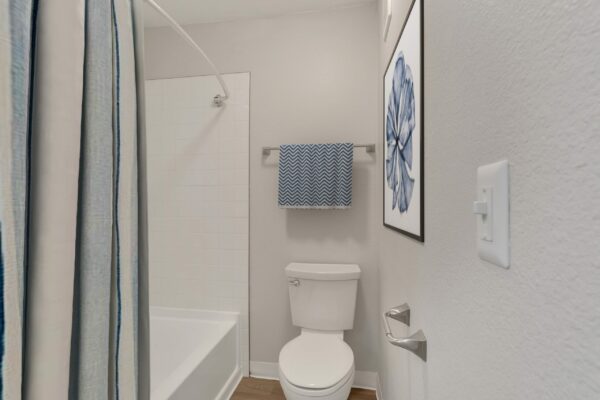 Bathroom with wood floor, framed artwork, and tiled shower tub.