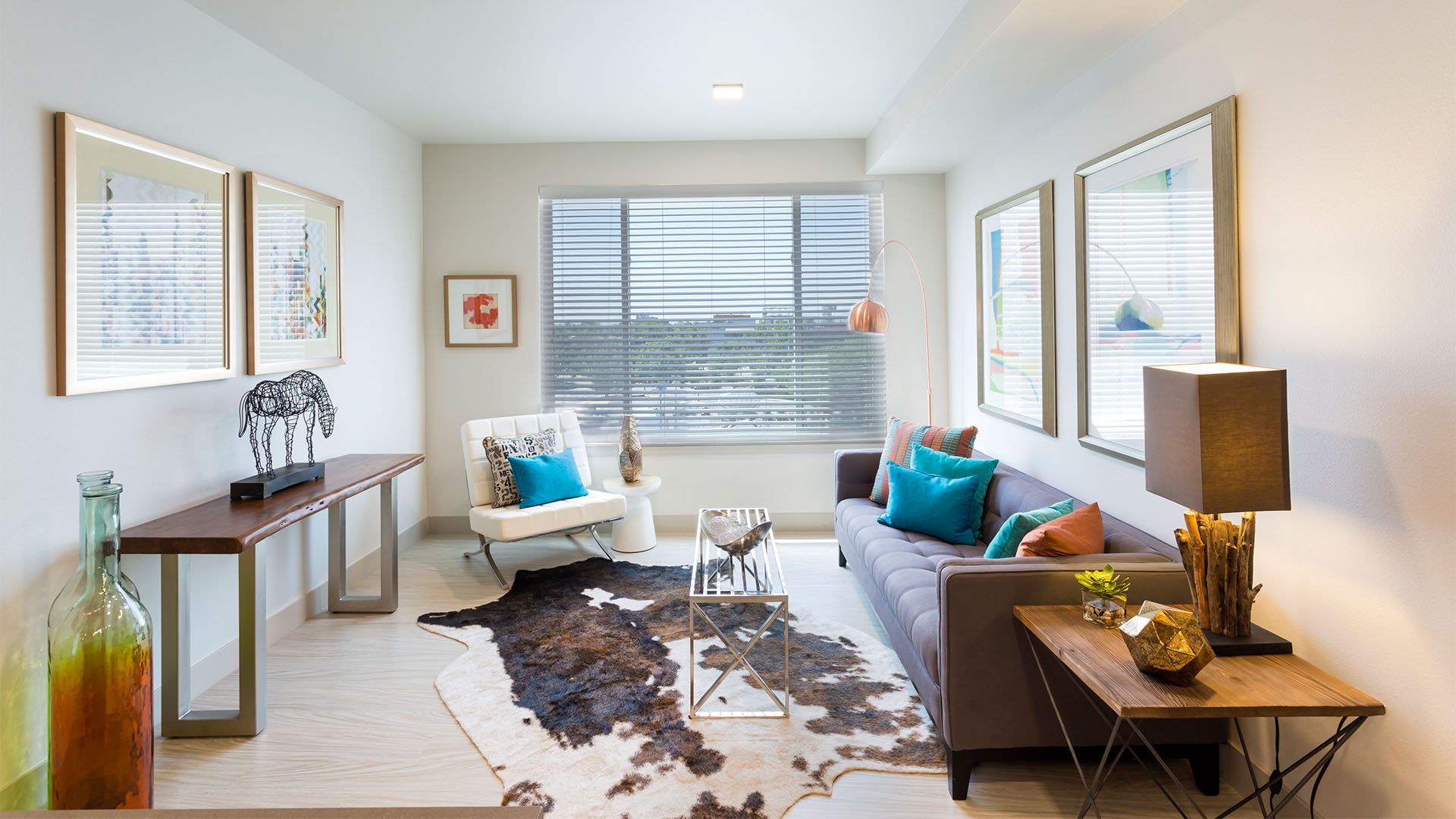 Living room with wood floor, modern furniture, framed artwork, sculptures, and large window.