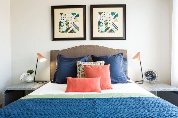 Bedroom with large platform bed, plush bedding, metal bedside tables, and geometric artwork.