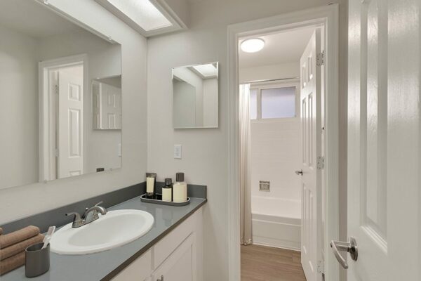 Bathroom with tile, white cabinets and counter, large mirror, and tiled shower tub with curtain.