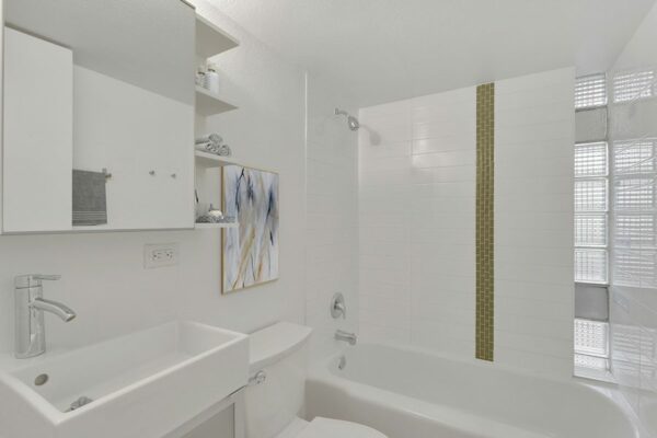 Bathroom with white sink basin, shelves, framed mirror, and tiled shower tub.