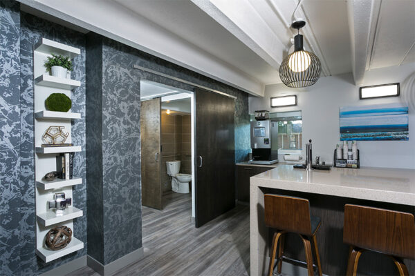 Coffee bar with wood floor, bar top with stools, coffee machine, and shelves with decor.