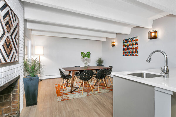Living area with wood floor, dining table, kitchen island with sink, and colorful artwork.