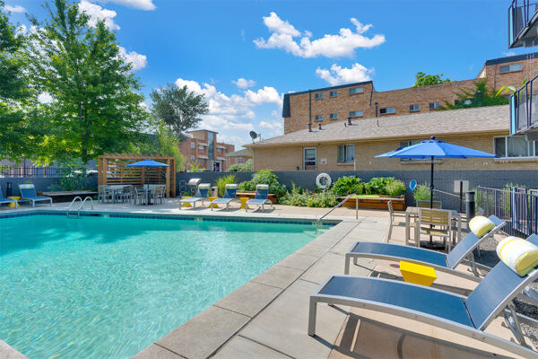 Pool area with lounge chairs, umbrellas, and tall trees.