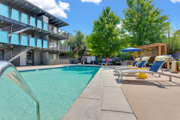 Pool area with bright blue water and lounge chairs overlooked by apartment balconies.