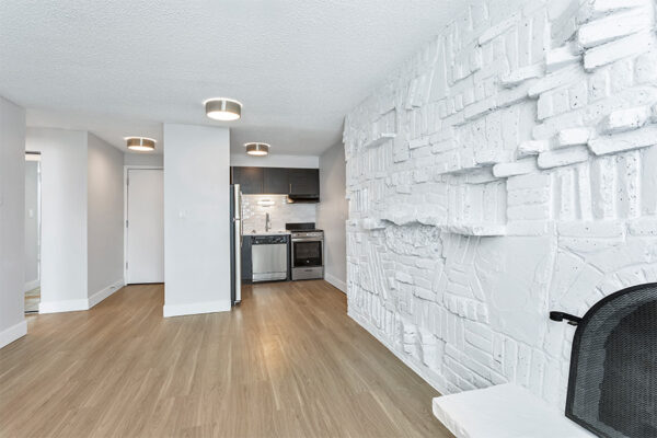 Living area with wood floor, white brick accent wall, and entry to kitchen.