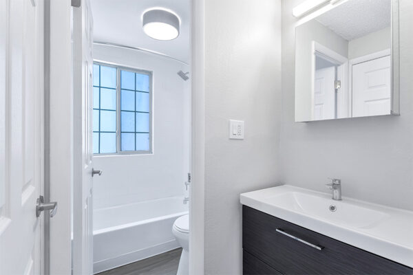 Bathroom with wood floor, dark cabinet, light counter, medicine cabinet, and tiled shower tub.