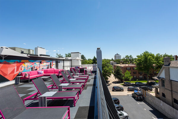 Rooftop patio with lounge chairs, outdoor couches, and mural art overlooking Denver.