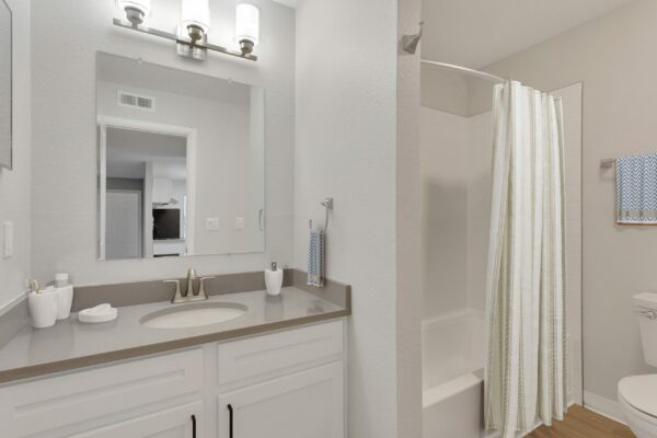 Bathroom with white cabinets, grey counters, large mirror, and tiled shower tub.