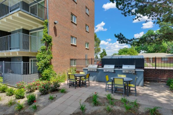 Outdoor grilling area with dining tables, built in BBQ grills, and lush landscaping.