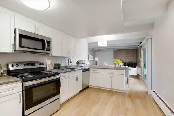 Kitchen with wood floor, white cabinets, stone counters, and stainless steel appliances.