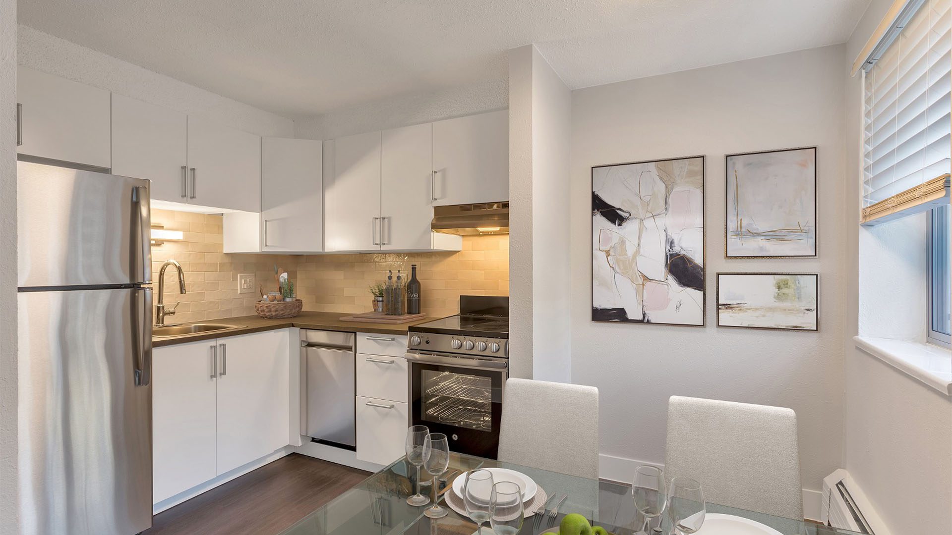 Apartment kitchen with wood floor, white cabinets, and stainless steel appliances.