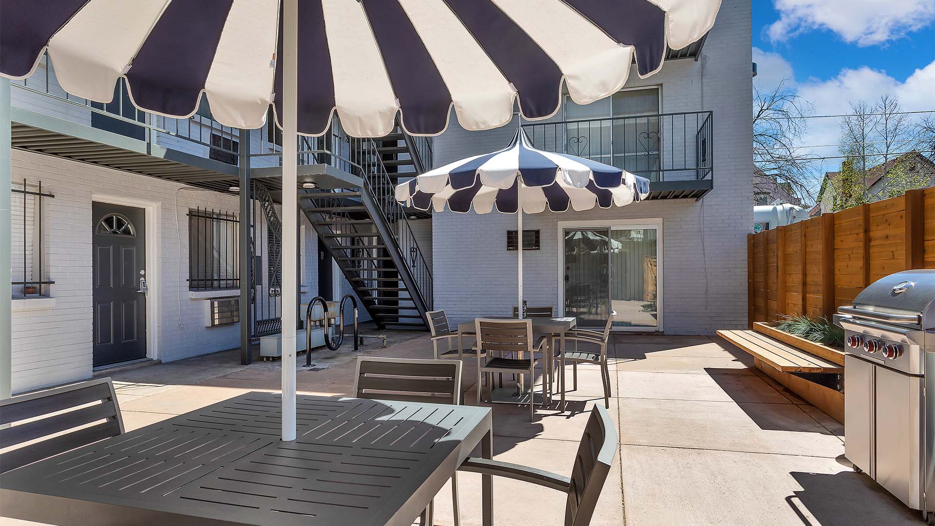 Patio with dining tables and BBQ grill overlooked by apartment balconies.