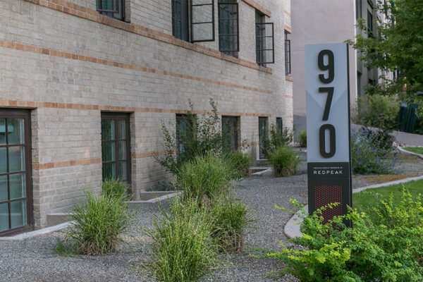 970 Penn monument sign with lush landscaping in front of blonde brick building.