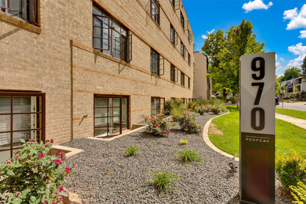 970 Penn monument sign with lush landscaping in front of blonde brick building.