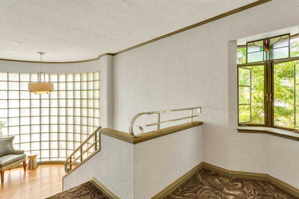 Stairwell landing with gold trim accents, round glass brick wall, and window with stained glass.