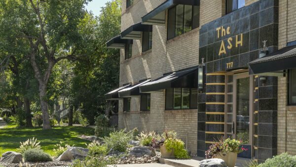 The Ash building with blonde brick construction, art deco tiled entry door, and lush landscaping.