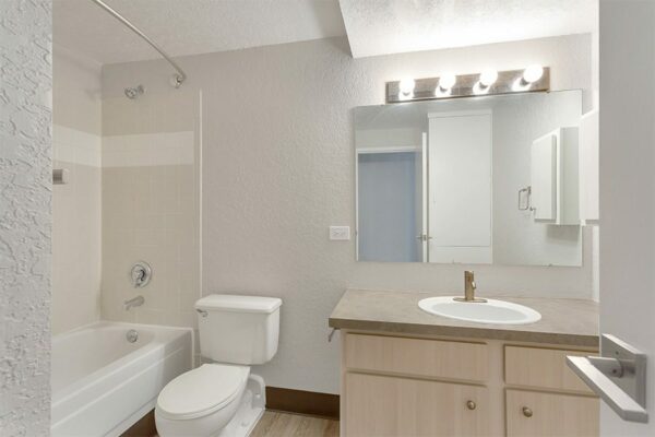 Bathroom with wood cabinets, tan counters, large mirror, and tiled shower tub.