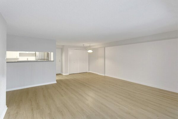 Living area with wood floor, grey walls, white trim, and opening to kitchen.
