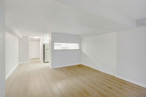 Living area with wood floor, grey walls, white trim, opening to kitchen, and door to hallway.