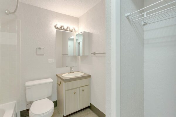 Bathroom with wood cabinets, tan counter, large mirror, medicine cabinet, and tiled shower tub.