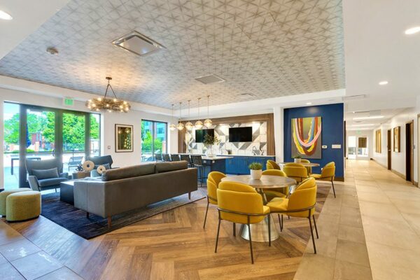 Lounge with wood and tile floors, comfortable modern furniture, wall mounted TVs, and large artwork.