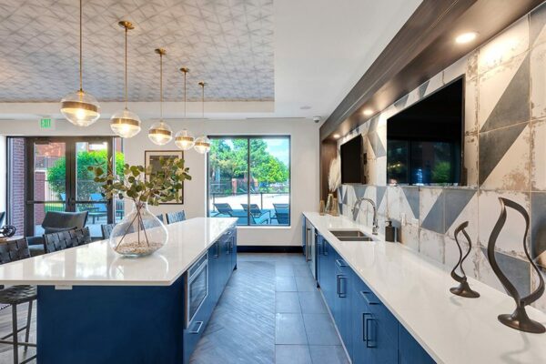Community kitchen with blue cabinets, white counters, breakfast bar, wall mounted TVs, and decorative lighting fixtures.