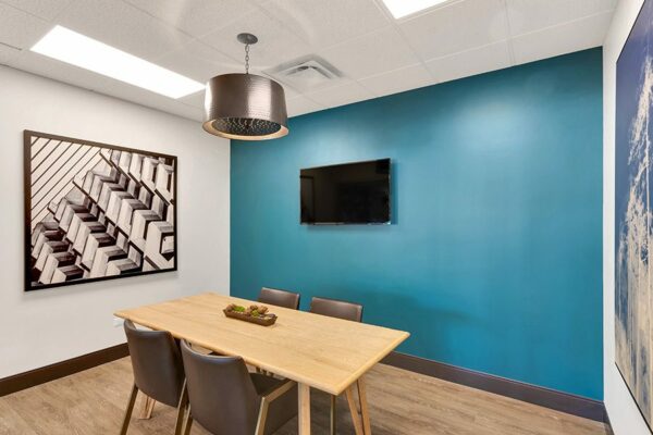 Meeting room with wood floor, blue accent wall, wood table with chairs, and wall mounted TV.