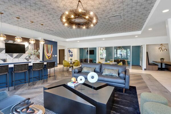 Lounge with comfortable modern furniture, decorative chandelier, and community kitchen with breakfast bar.