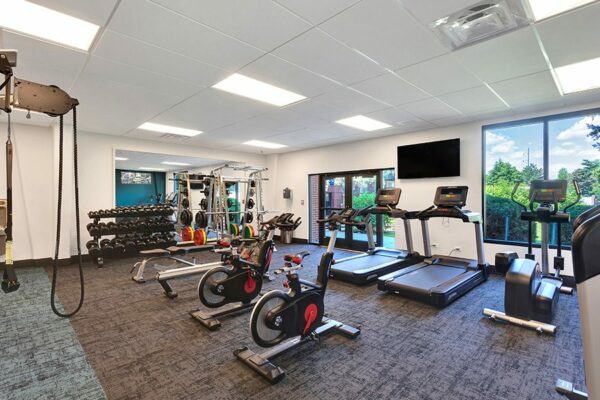 Fitness center with carpet, cardio machines, weight equipment, wall mounted TV, and large windows.