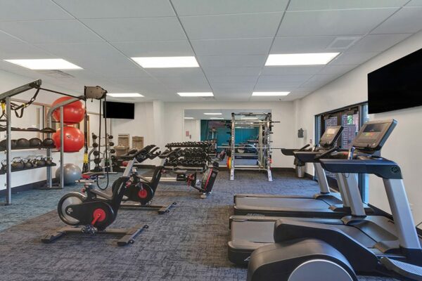 Fitness center with carpet, cardio machines, weight equipment, wall mounted TV, and large windows.