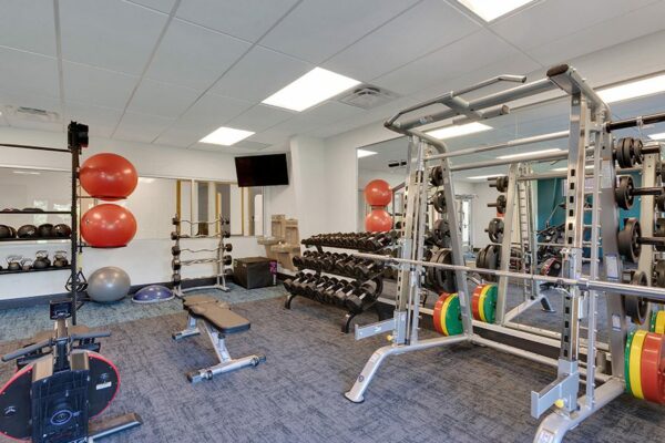Fitness center with mirror walls, wall mounted TV, and weight lifting equipment.